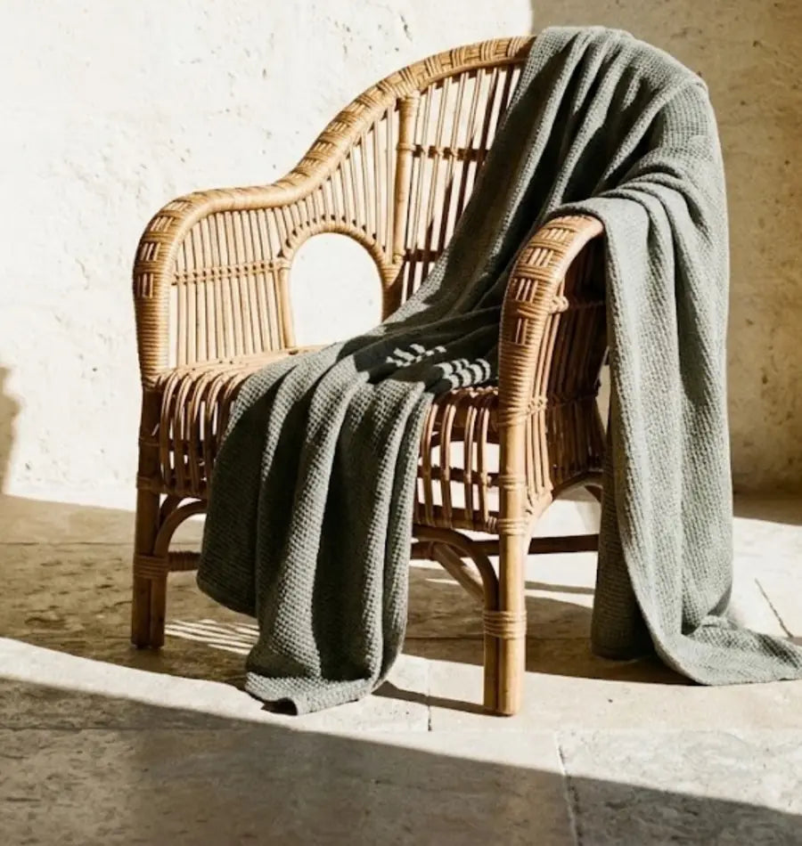 Rattansessel mit graugrüner Decke im Sonnenlicht